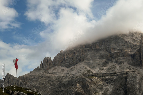 A Tirolian flag waving on a wind in Italian Dolomites. There are many high and sharp peaks covered with light clouds. Dangerous landslides, with many lose stones around. Raw and unspoiled landscape. photo