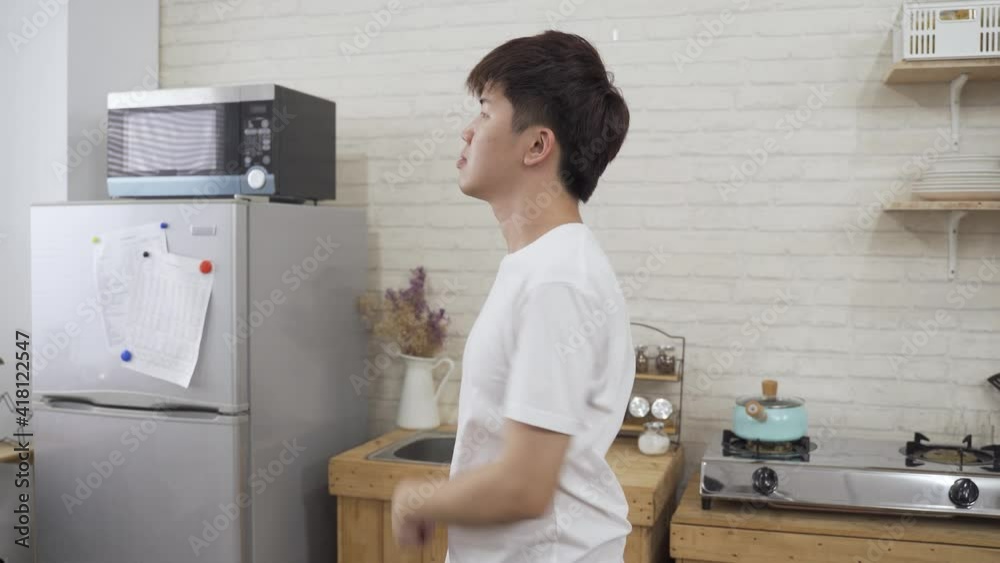side portrait young Asian man is doing simple exercise by rotating his neck and turning upper body to relax at modern home kitchen background.