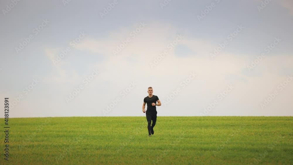 A sportsman is running across the green grass and looking at the camera. Running training. 4K. A sportsman is running across the green grass and looking at the camera. Running training. 4K.
