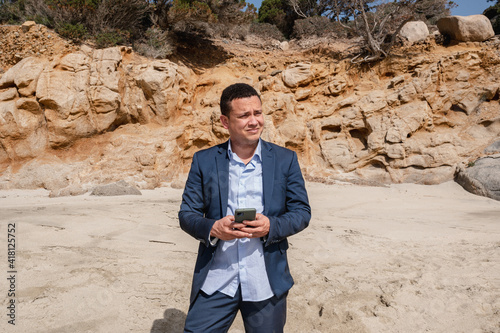 Latin man in elegant suit at the beach using smartphone and looking away. Escape from the city searching peaceful place photo