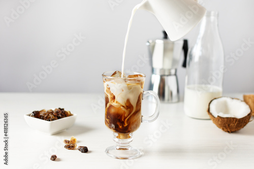 Pouring coconut milk into glass with iced coffee.