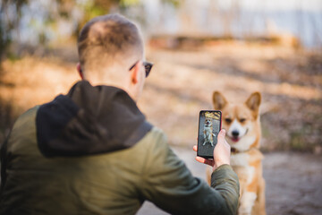 youg man taking a photo of his welsh corgi pembroke dog doing a trick