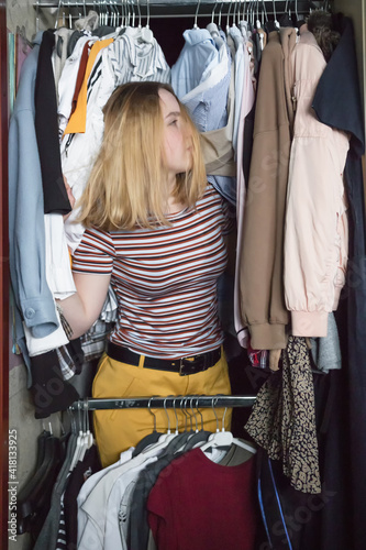 Spring cleaning,Fast fashion, the girl puts things in order in the closet. A bunch of colorful clothes. The concept of processing, second hand, eco, minimalism, consumption of goods..