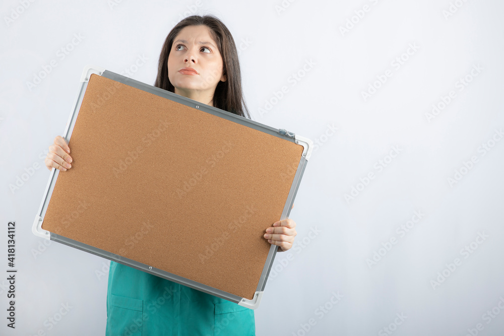 Thoughtful young nurse holding board and looking up Thoughtful young nurse holding board and looking up