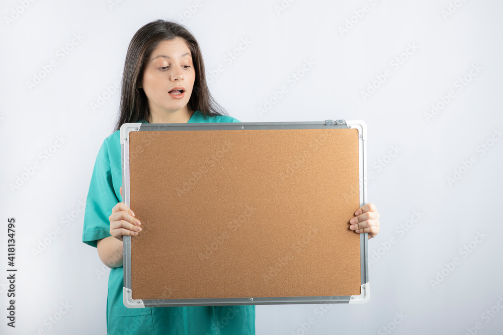 Shocked medical worker holding board and pointing finger on it Shocked medical worker holding board and pointing finger on it