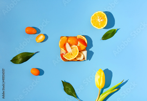 Fototapeta Naklejka Na Ścianę i Meble -  A bright composition, sandwitch with fresh organic citrus fruits, lemons, kumquats, slices of pear and banana, on a cyan background. Healthy spring concept.