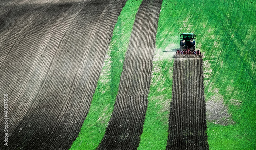 Принти на полотні Sunshine view of big tractor plowing the ground of green field on the slope