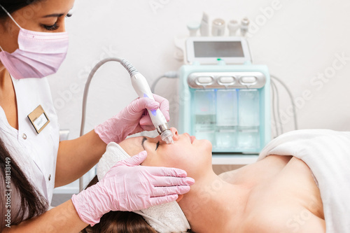 Beauty salon. The cosmetologist in medical gloves doing a hydra peeling procedure on the client's cheeks. Side view. Cloe up of device. Professional skin care and beauty concept
