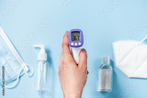 Showing temperature on a blue background with surgical masks. Hand showing thermometer on light background