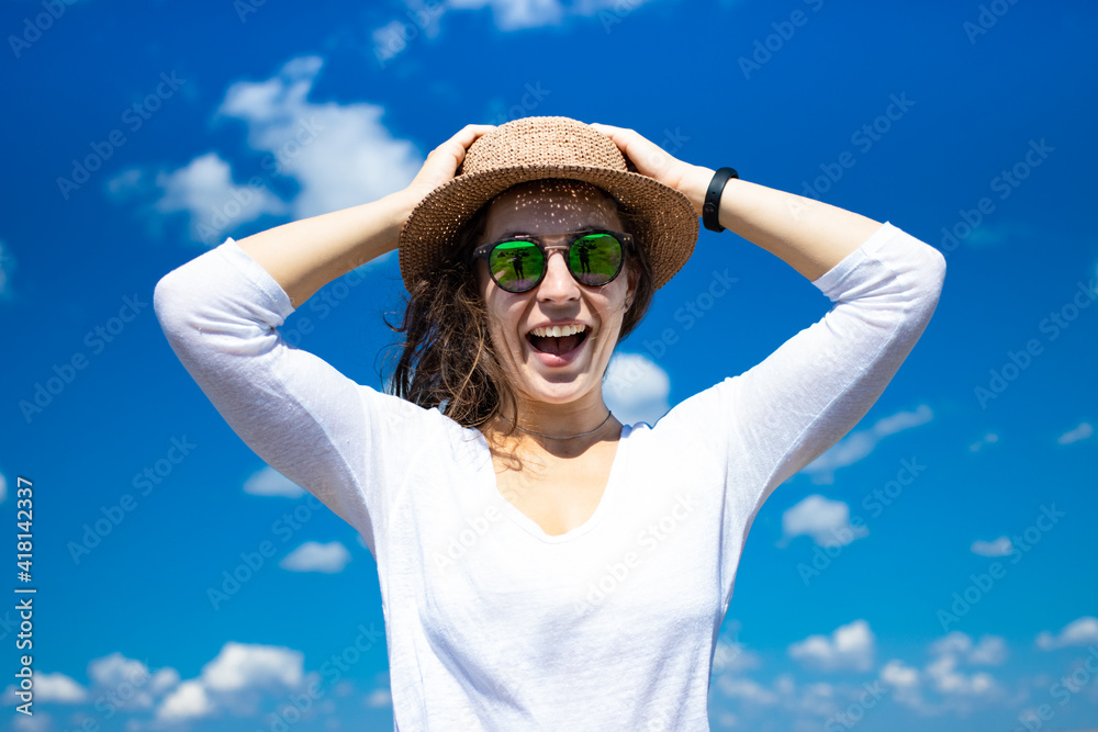 Excited happy young woman in summer hat holding head by two hands opening her mouth in amazement, wearing sunglasses and white t-shirt on blue sky background.Tourist girl astonished receive good news Excited happy young woman in summer hat holding head by two hands opening her mouth in amazement, wearing sunglasses and white t-shirt on blue sky background.Tourist girl astonished receive good news
