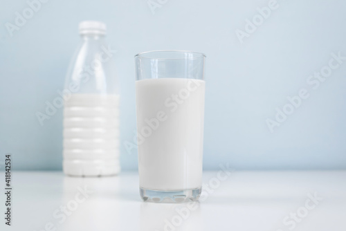 Glass of milk and bottle standing on white table, indoors. Morning healthy breakfast concept. Minimalistic photo.