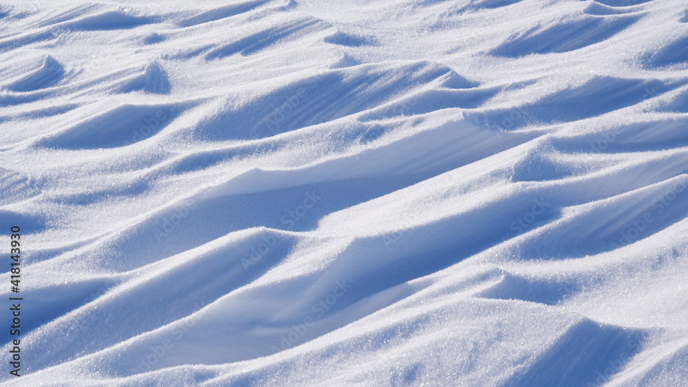 The background is a snowy shiny surface in the shape of waves. Part of the image is blurred. The background is a snowy shiny surface in the shape of waves. Part of the image is blurred.