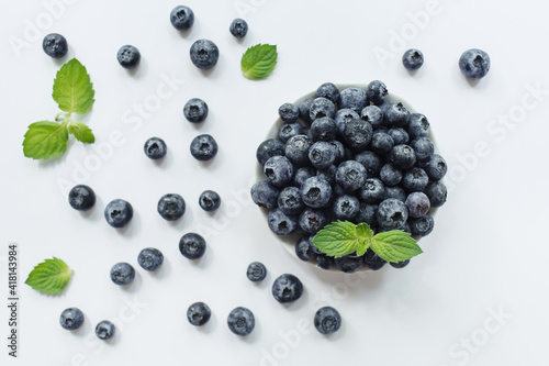 Fresh blueberries in white bowl and green leaves on white background. Flat lay, top view.