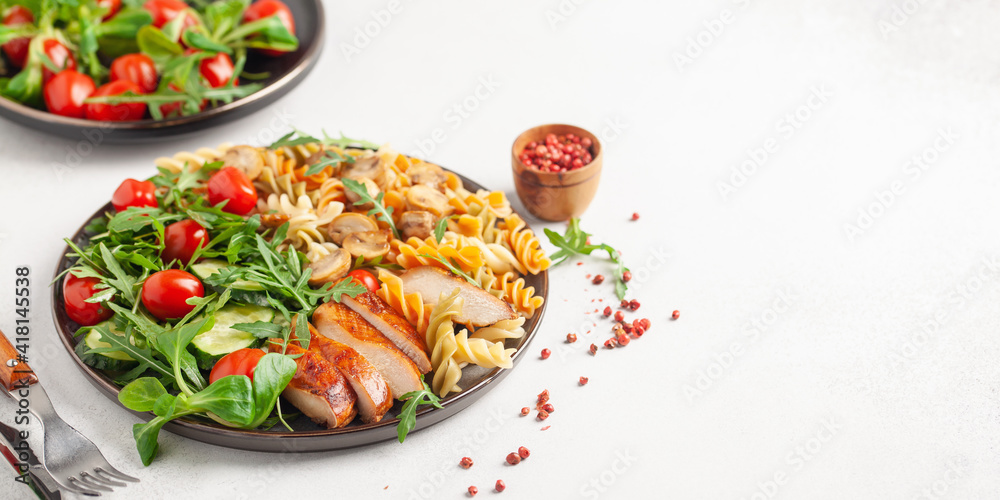 Grilled chicken breast, pasta fusilli, arugula, tomatoes, cucumber slice and mushrooms  in plate.
