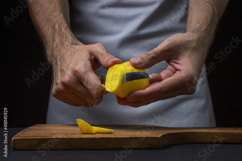 Potatoes on a dark background. The cook cuts the potatoes with a knife. Male hands cut potatoes on black background