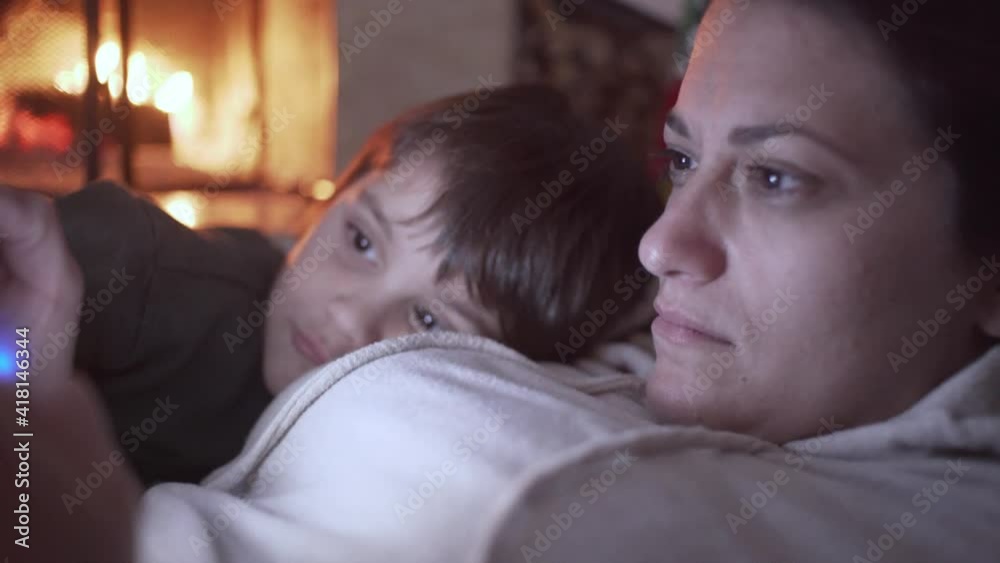 Close up shot of caucasian mother playing console video game,while here son watching and laughing besides her. Fireplace burning in the blurry background Close up shot of caucasian mother playing console video game,while here son watching and laughing besides her. Fireplace burning in the blurry background