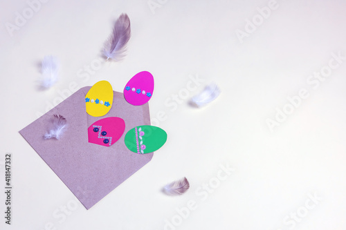 a kraft paper envelope with Easter eggs made of paper and bird feathers on a yellow background. easter greeting card