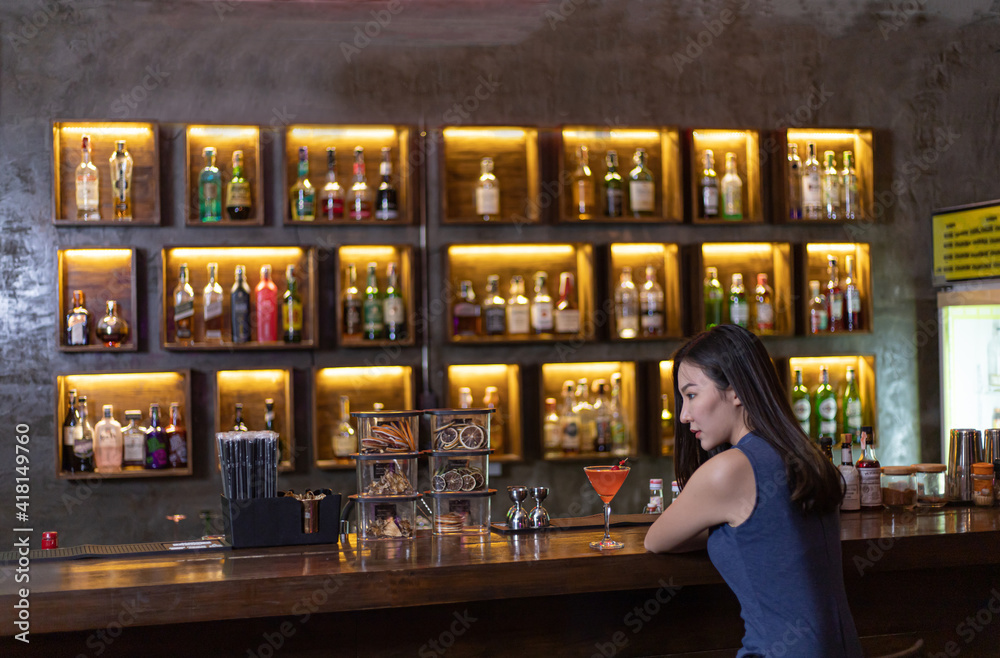 Young Asian woman with a sad face drinking cocktails in front of a vintage bar, Relaxing activities after work or hangouts, Place of entertainment for young adolescents or night club party.
