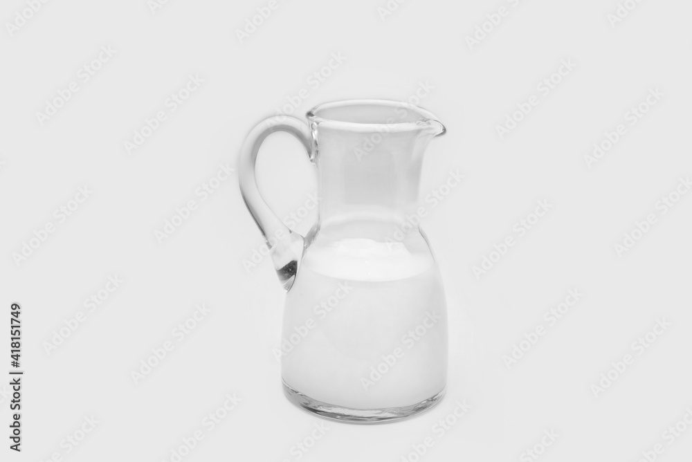 Glass pitcher half full with milk on a white background Glass pitcher half full with milk on a white background