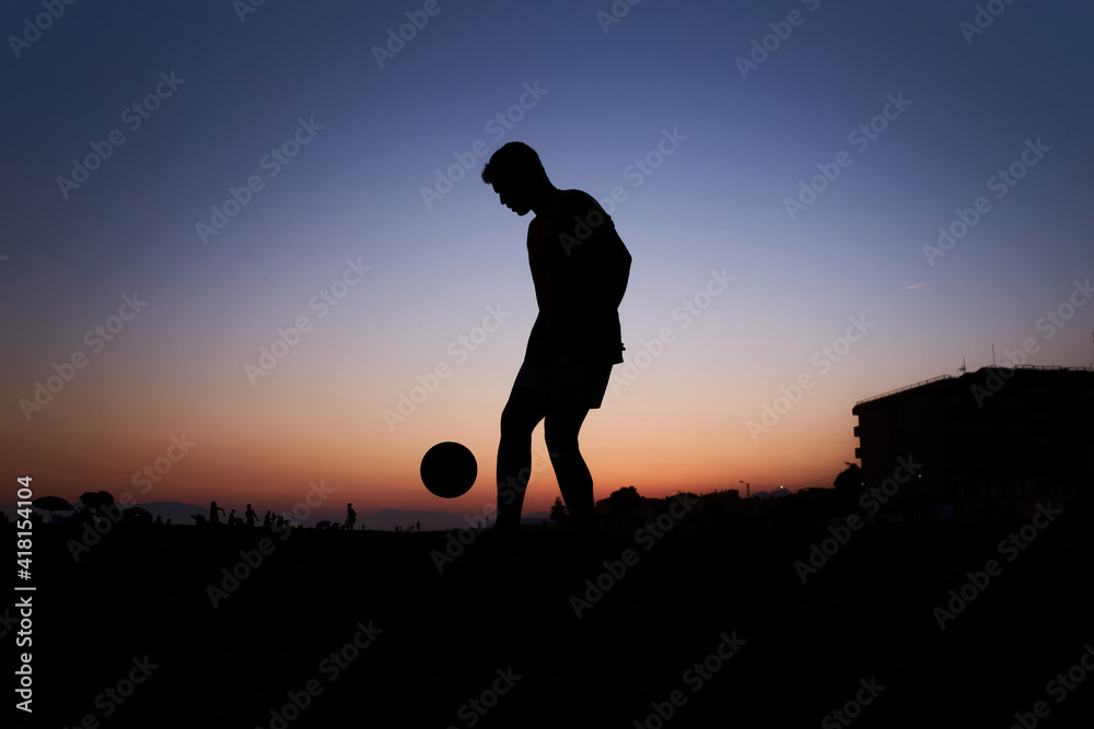 Silhouette of young man playing soccer on the beach with a ball at sunset Silhouette of young man playing soccer on the beach with a ball at sunset