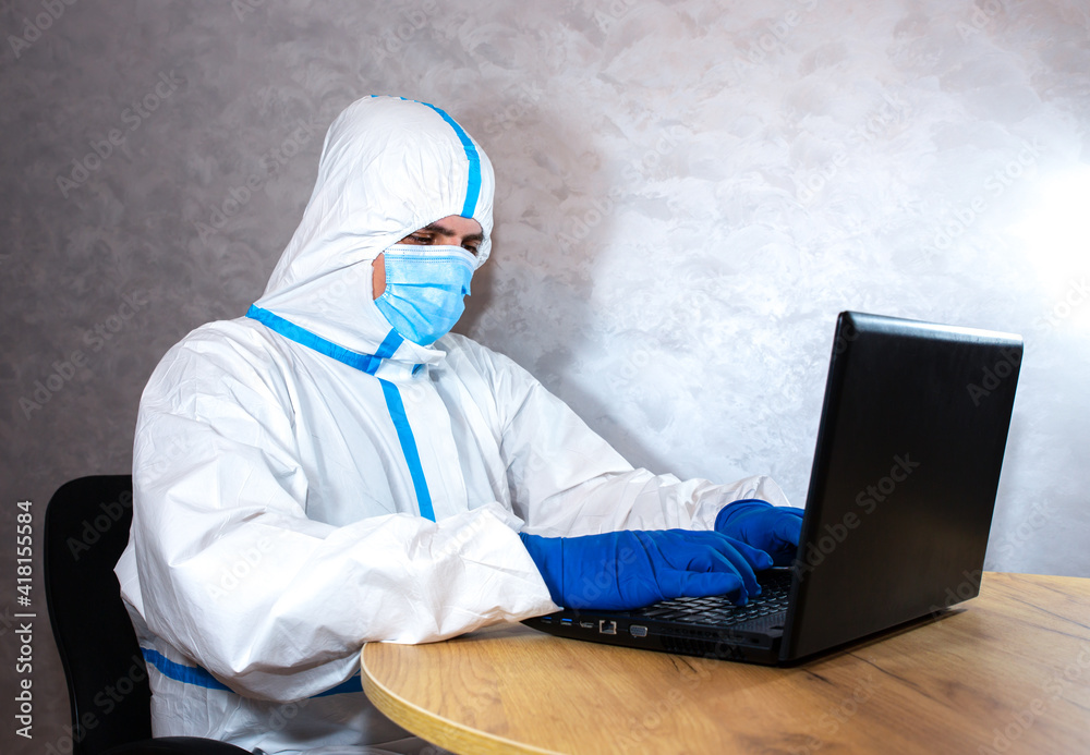 Doctor wearing medical protective suit, medical mask and gloves working on laptop. Protection mers by virus epidemic. Coronavirus (COVID-19). Healthcare concept. Remote work in a pandemic covid. Doctor wearing medical protective suit, medical mask and gloves working on laptop. Protection mers by virus epidemic. Coronavirus (COVID-19). Healthcare concept. Remote work in a pandemic covid.