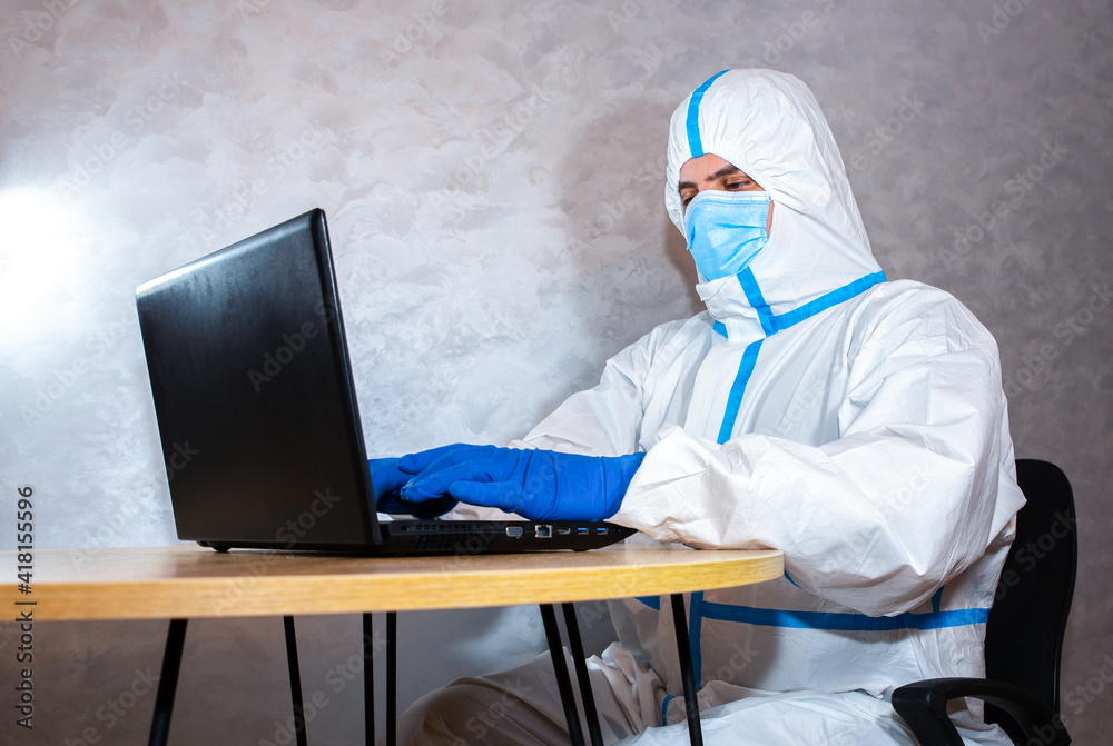 Doctor wearing medical protective suit, medical mask and gloves working on laptop. Protection mers by virus epidemic. Coronavirus (COVID-19). Healthcare concept. Remote work in a pandemic covid. Doctor wearing medical protective suit, medical mask and gloves working on laptop. Protection mers by virus epidemic. Coronavirus (COVID-19). Healthcare concept. Remote work in a pandemic covid.