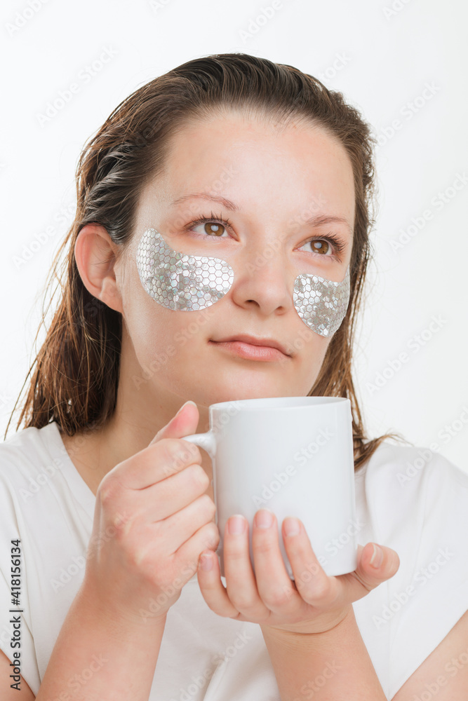 Beautiful woman with cup and collagen pads under her eyes. Morning routine