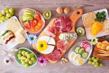 Spring or Easter theme charcuterie table scene against a wood background. Variety of cheese, meat, fruit and vegetable appetizers. Top view.
