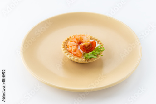 Tartlet with shrimp, tomato and greens on a plate.