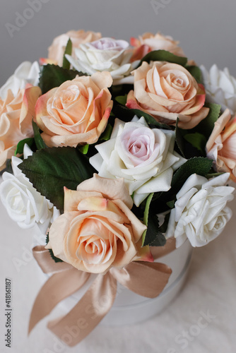 Artificial roses in a round box on a white table  close-up. Decorative bouquet of flowers.