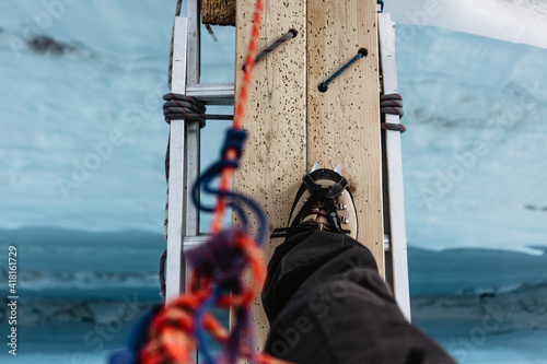 person crossing over a glacier crevasse at mt rainier in the united states of america while wearing climbing boots and rope on a ladder on mount rainier doing mountain climbing crampons and safety 