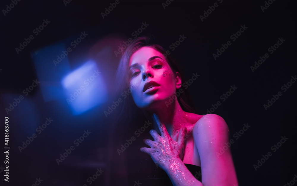 Trendy night wear of a woman with make-up in glitter on her face and hands posing for the camera in violet light with blue highlights.