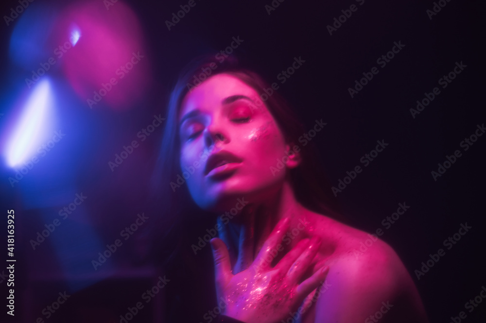Background. Blurred abstract photo of a woman with glitter on her face dancing out of focus in a dark room with purple and blue light. Background. Blurred abstract photo of a woman with glitter on her face dancing out of focus in a dark room with purple and blue light.