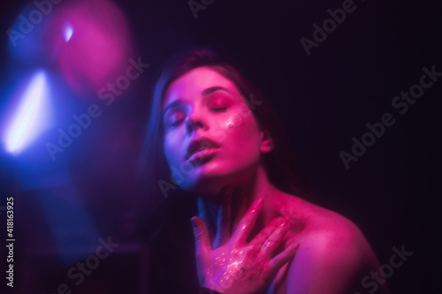 Background. Blurred abstract photo of a woman with glitter on her face dancing out of focus in a dark room with purple and blue light.