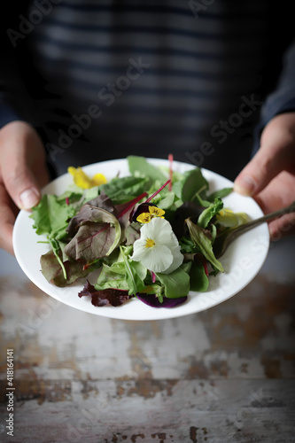 Soft focus. Hands hold healthy salad with flowers on a plate. Diet concept.