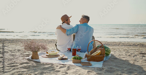 Homosexual lgbt couple, gay men having picnic at the beach, sitting on blanket and embracing, looking to ech other with love photo