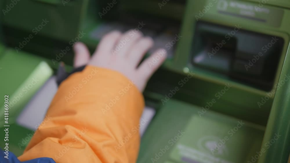 Withdraw money from an ATM. The child withdraws cash from the cash dispenser. Defocusing. Withdraw money from an ATM. The child withdraws cash from the cash dispenser. Defocusing.