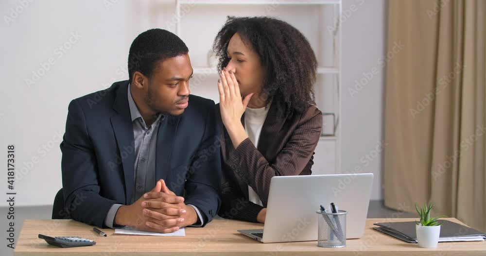 Two afro american men sitting at table in office businesswoman telling secret to businessman whispering into male ear bad news gossip manager guy feeling sad frustration stress hears about dismissal Two afro american men sitting at table in office businesswoman telling secret to businessman whispering into male ear bad news gossip manager guy feeling sad frustration stress hears about dismissal