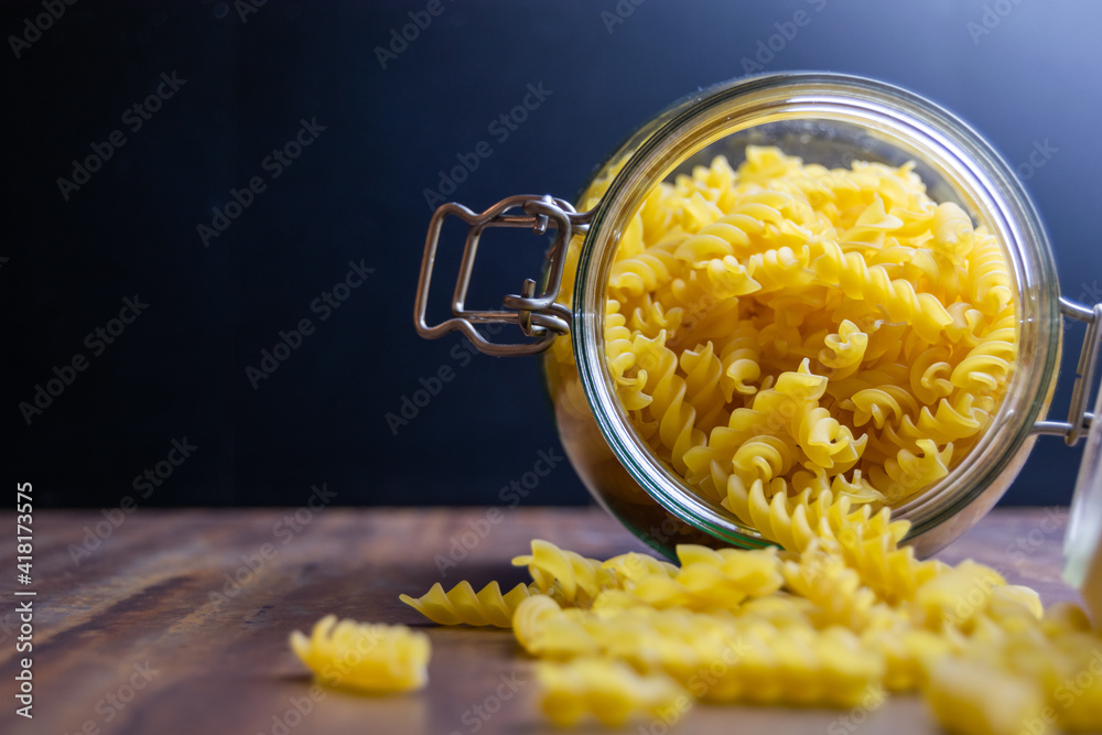 Fussili pasta falling out from a big air tight glass jar. Raw dry pasta