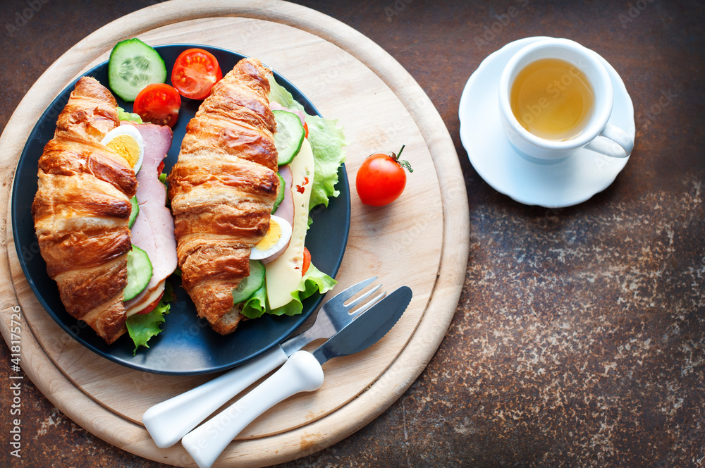 Croissant sandwich with ham, cheese, fresh salad, tomatoes, eggs and cucumber on wooden background. Breakfast with fresh croissant sandwich. Top view
