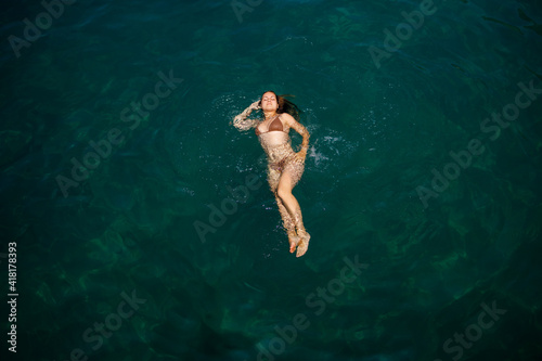 A beautiful young attractive woman in a swimsuit lies on the surface of the water at the sea. View from above. She is enjoying her vacation. Selective focus