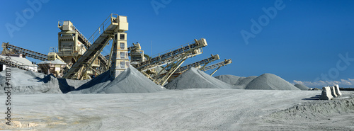 Quarry machines and piles of gravel over blue sky. Stone crushing and screening plant, panoramic view photo