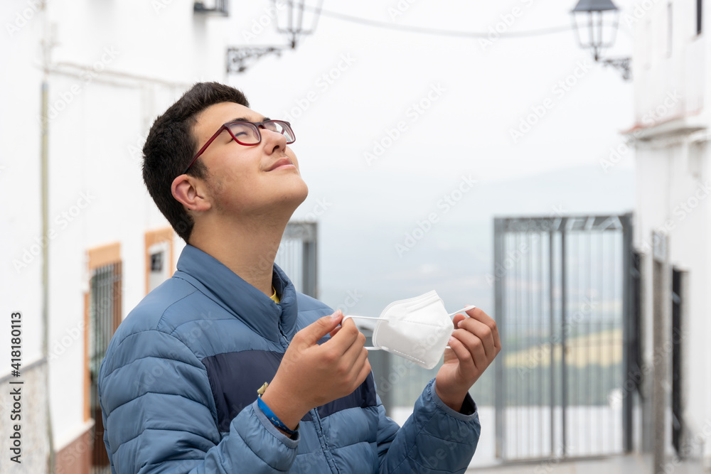 Young boy wearing glasses deep breathing and taking his face mask off in the street. Young boy wearing glasses deep breathing and taking his face mask off in the street.