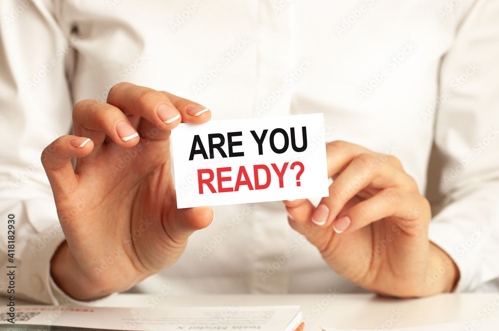 A woman in a white shirt holds a piece of paper with the text: ARE YOU READY. Business concept. A woman in a white shirt holds a piece of paper with the text: ARE YOU READY. Business concept.