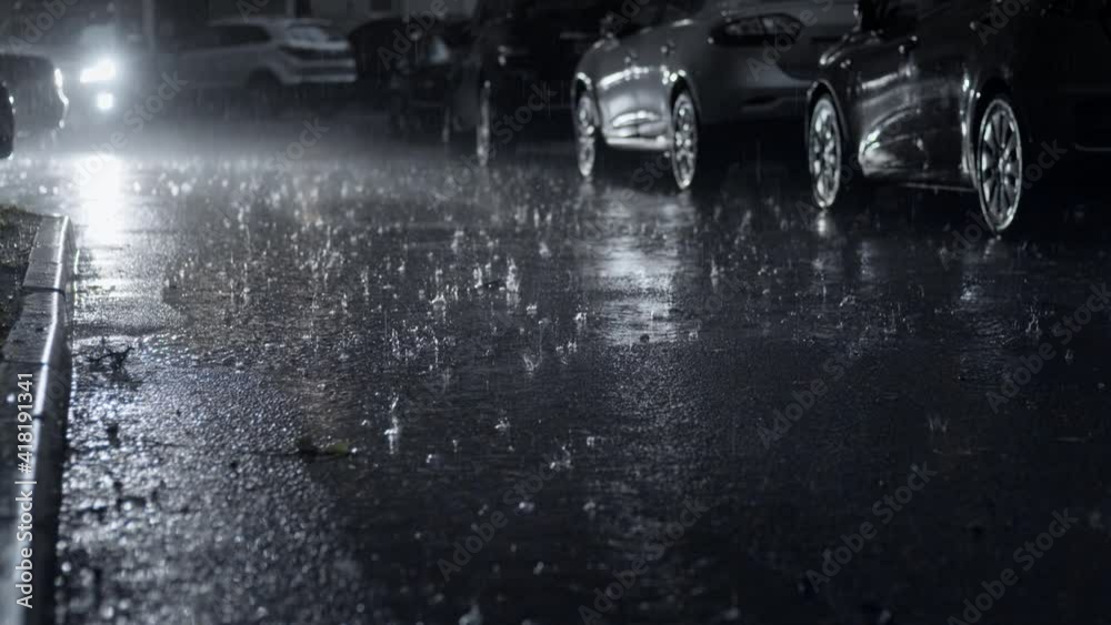 Pouring rain in the dark city yard at night. Selective focus on the asphalt road with raindrops. Static camera