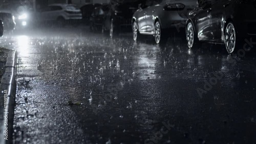 Pouring rain in the dark city yard at night. Selective focus on the asphalt road with raindrops. Static camera