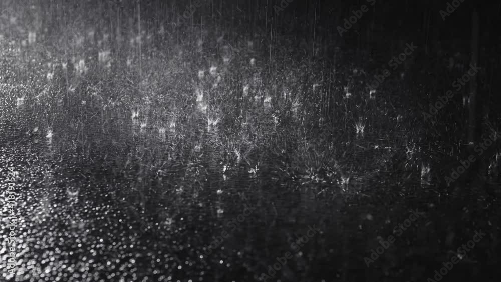 Dark asphalt road under pouring rain. Selective focus on the surface and raindrops. Static camera
