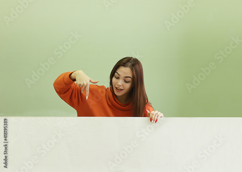 Beautiful young cheerful surprised girl shows down. Place for advertising.