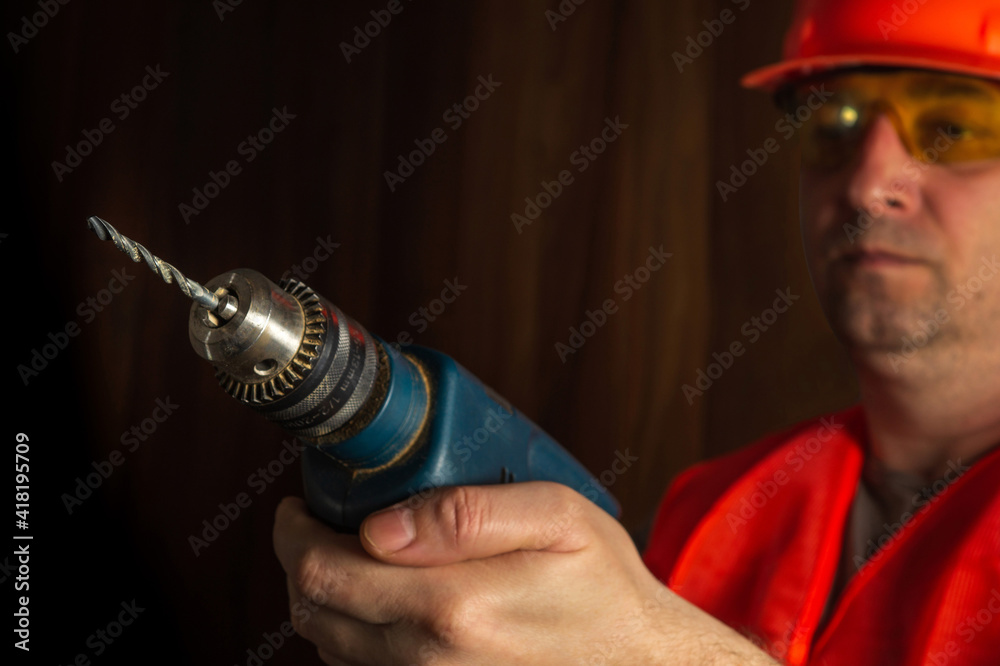 Woodworker holds an electric drill close-up during carpentry work. Working environment in a carpentry workshop