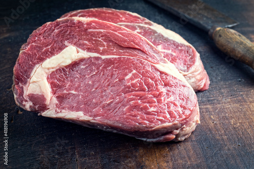 Raw dry agd angus rib-eye beef steak offered as close-up on a rustic burnt wooden board photo